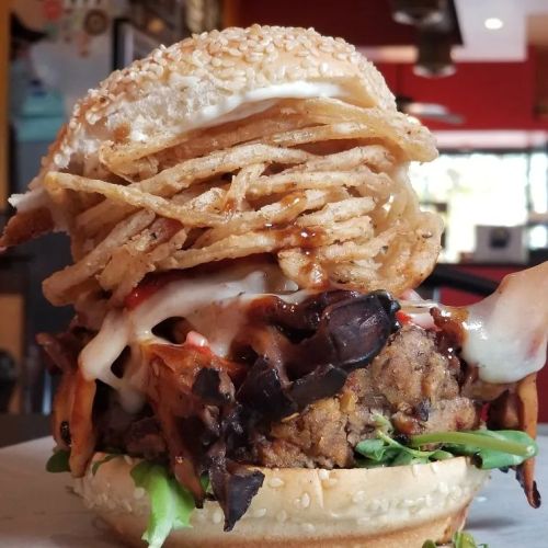 A close-up of a burger topped with crispy onions, sauce, and lettuce, served in a sesame seed bun.