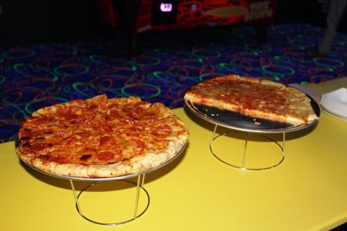 Two pizzas on stands: one with pepperoni and the other with cheese, set on a bright yellow table.