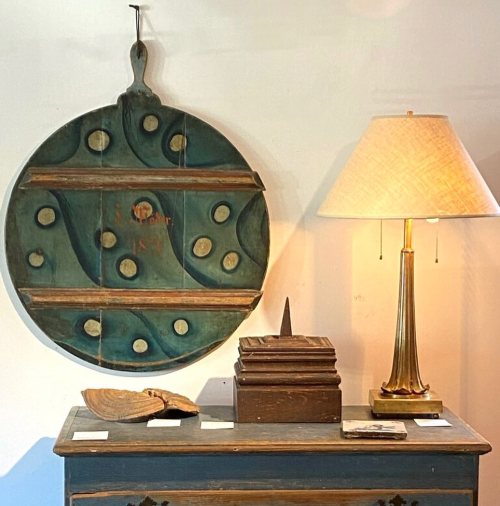A decorative wooden wall piece with circular design, a lamp, and various wooden objects on a table.
