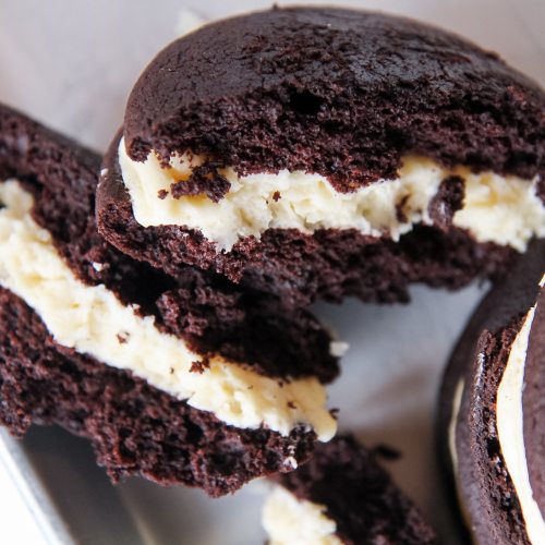 Close-up of chocolate whoopie pies filled with creamy white filling, partially cut to show the inside texture.