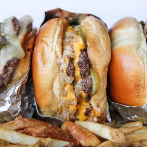 Two burgers with melted cheese, pickles, and onions, served with a side of golden fries.
