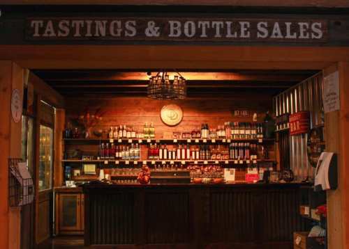 A rustic wine tasting and bottle sales counter with shelves of bottles and a warm wooden interior.
