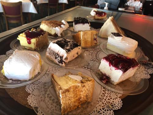 A tray of assorted cakes and cheesecakes, each topped with cream and fruit, displayed on lace doilies.