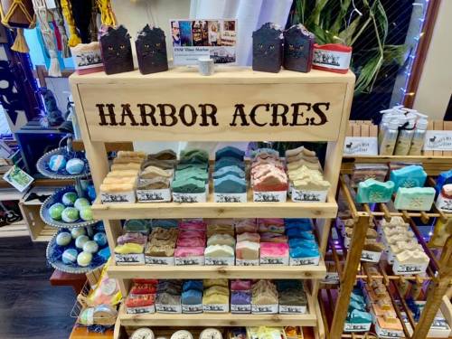 A wooden display shelf labeled "Harbor Acres" showcasing various colorful soaps and bath products in a shop.