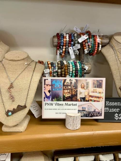 Display of handmade jewelry and bracelets at PNW Vibes Market, featuring a sign with market details and photos.