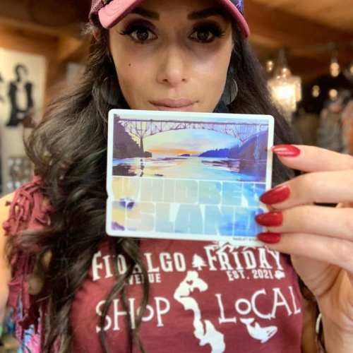 A woman in a cap holds a postcard featuring a scenic landscape, smiling at the camera.
