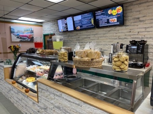 A counter in a café displaying baked goods, drinks, and a menu on screens above, with a floral arrangement nearby.