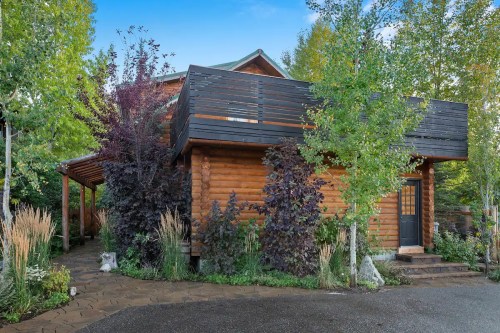A modern wooden house surrounded by lush greenery and colorful shrubs, with a stone pathway leading to the entrance.