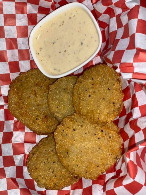 A basket lined with red and white checkered paper containing golden-brown fried patties and a small bowl of dipping sauce.