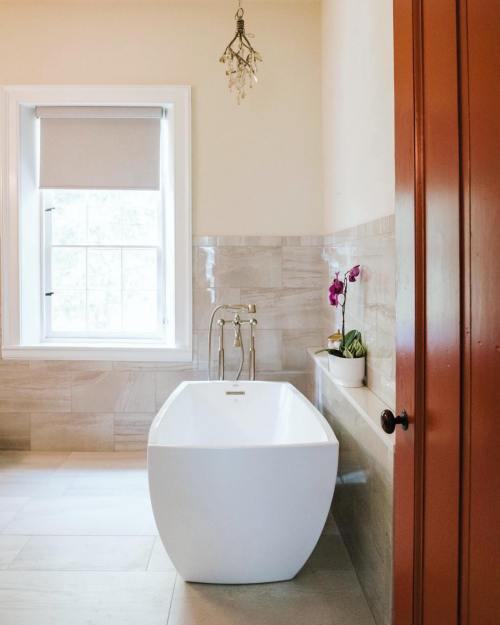 A modern bathroom featuring a freestanding white tub, a window with a shade, and a small orchid on the ledge.