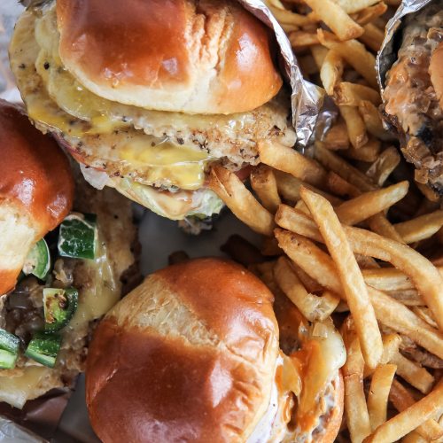 A close-up of two burgers with toppings and a side of golden French fries.