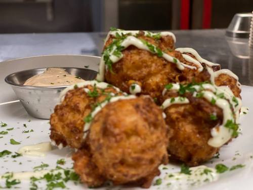 Crispy golden fritters topped with herbs and drizzled with sauce, served with a small bowl of dipping sauce.