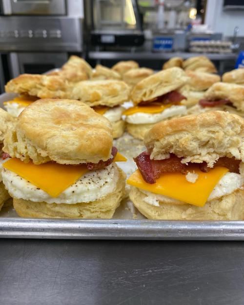 A tray of freshly made breakfast biscuits with cheese, eggs, and bacon stacked neatly.