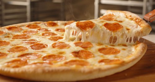 A freshly baked pepperoni pizza with gooey cheese, one slice being lifted, revealing its stretchy cheese.