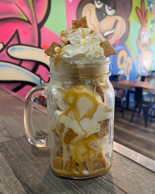 A mason jar filled with layers of whipped cream, cereal, and caramel sauce, set against a colorful graffiti background.
