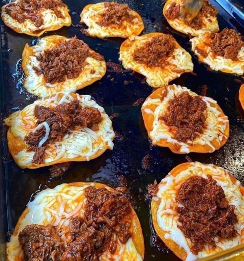 A close-up of golden tortillas topped with melted cheese and shredded beef, sizzling on a griddle.
