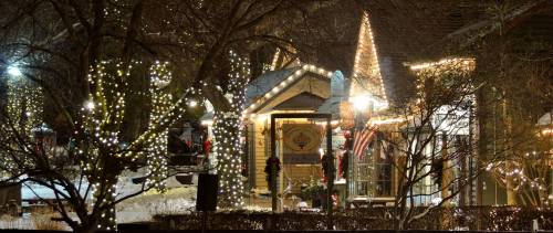 A cozy winter scene featuring a warmly lit building adorned with holiday lights and decorations amidst snowy trees.
