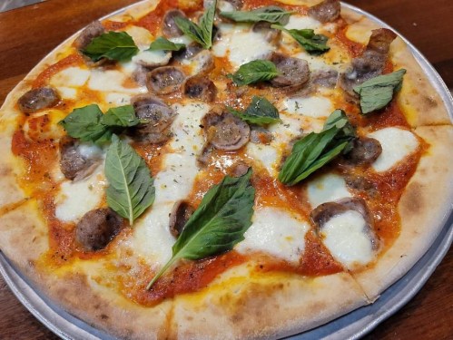 A freshly baked pizza topped with mozzarella, sausage, and fresh basil leaves on a metal tray.
