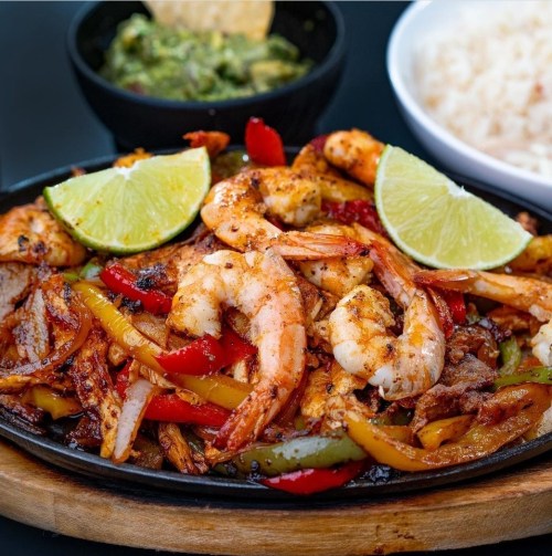 Sizzling shrimp fajitas with colorful peppers, served with lime wedges, guacamole, and rice on the side.