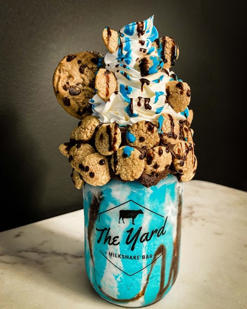 A tall milkshake topped with whipped cream, chocolate drizzle, and mini cookies in a jar from The Yard Milkshake Bar.