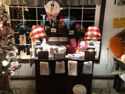 A cozy shop display with festive decorations, lamps, and holiday-themed items on a table near a window.