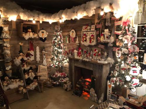 Cozy holiday scene with decorated trees, snowman decorations, and a fireplace surrounded by festive ornaments.