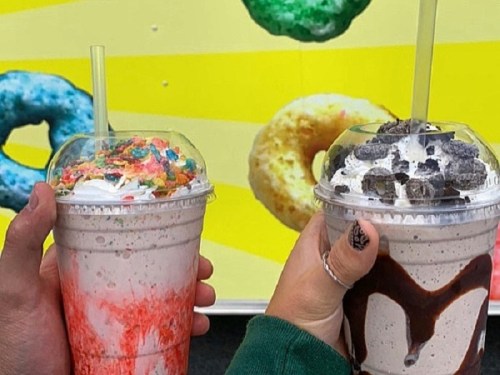 Two colorful milkshakes in clear cups, one topped with sprinkles and the other with chocolate syrup and cookies.