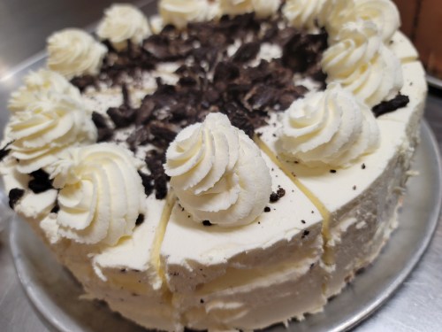 A round cake topped with whipped cream swirls and chocolate crumbs on a silver platter.