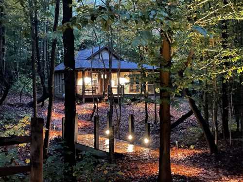 A cozy cabin illuminated at dusk, surrounded by trees and a path lit by soft lights.