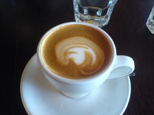 A cup of coffee with a creamy swirl design on top, placed on a white saucer.