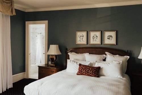 Cozy bedroom with a large bed, decorative pillows, and framed art on the wall; bathroom visible through an open door.