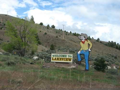 A colorful welcome sign for Lakeview featuring a cowboy figure against a hilly landscape with trees and clouds.