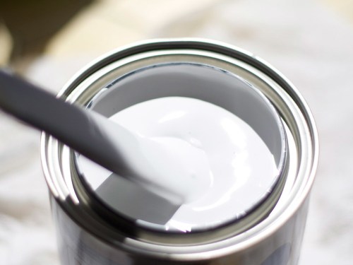 Close-up of an open paint can with white paint and a stir stick inside.