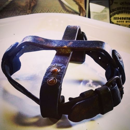 A vintage metal device with straps and rivets, resembling a restraint or harness, placed on a light surface.
