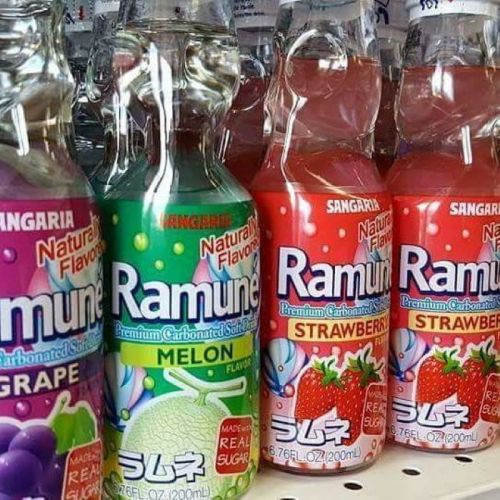 Three bottles of Ramune soda in grape, melon, and strawberry flavors, displayed on a shelf.
