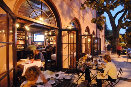 A cozy restaurant with outdoor seating, people dining, and warm lights glowing in the evening ambiance.