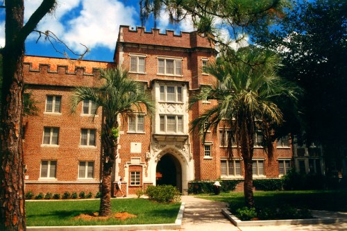 Historic brick building with a castle-like design, surrounded by palm trees and a blue sky.