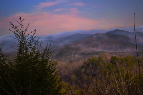 A serene mountain landscape at dusk, featuring rolling hills and a colorful sky with soft clouds.