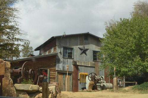 Rustic building with a metal exterior, a star decoration, and old machinery in front, surrounded by trees and cloudy skies.