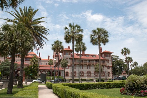 Historic building surrounded by palm trees and lush greenery under a blue sky with scattered clouds.