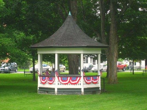 A gazebo decorated with red, white, and blue bunting, surrounded by green grass and trees.