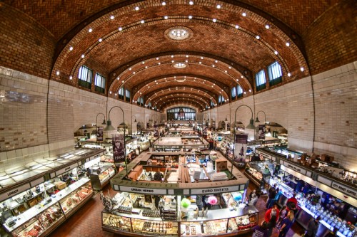 A bustling market interior with high arched ceilings, showcasing various food stalls and shoppers.