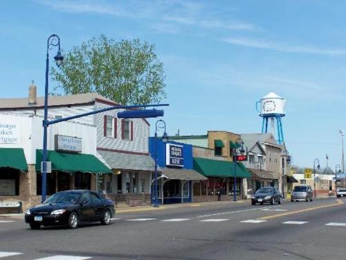 A small town street with shops, green awnings, and a water tower in the background under a clear blue sky.