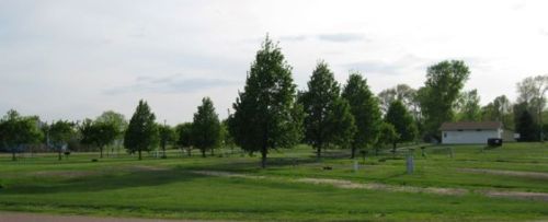 A grassy area with several trees and a small house in the background under a partly cloudy sky.