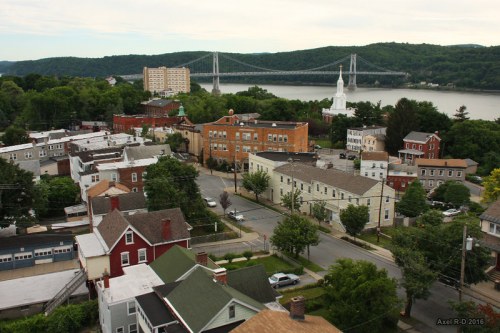 Aerial view of a small town with houses, trees, and a bridge over a river in the background.