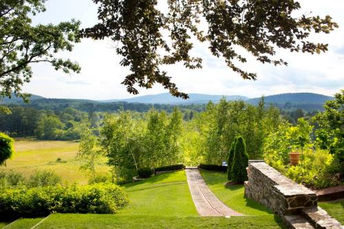 A scenic view of a lush green landscape with rolling hills, trees, and a stone pathway leading down.