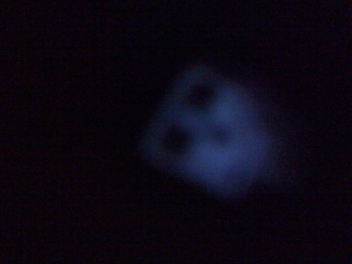 A blurred, dark image featuring a faintly illuminated object with two square shapes, possibly a face or a mask.