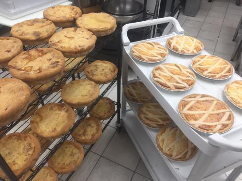 A variety of freshly baked pies cooling on racks and a cart in a kitchen setting.