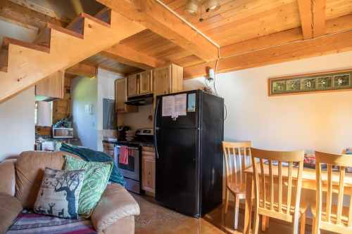 Cozy kitchen and dining area with wooden beams, a black fridge, and a staircase leading to an upper level.