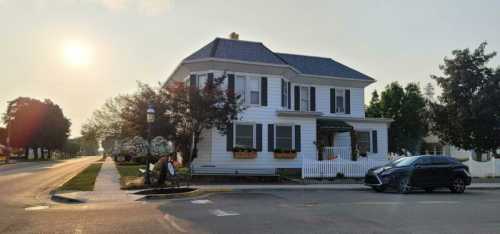 A charming white house with a dark roof, surrounded by trees, on a quiet street at sunset.